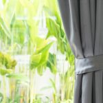 Imagem de uma janela com plantas ao fundo e cortina sobre a janela