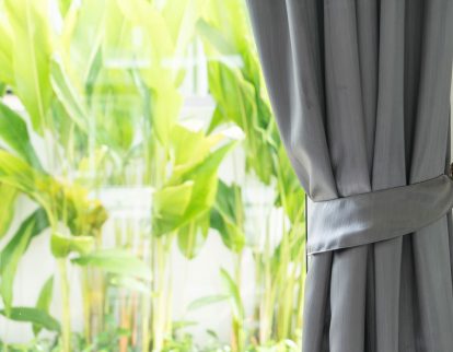 Imagem de uma janela com plantas ao fundo e cortina sobre a janela